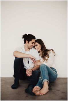 a man and woman are sitting on the floor with their arms around each other as they smile