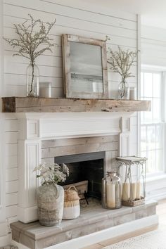 a fireplace with candles, vases and flowers on it's mantle in a white living room