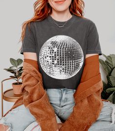 Revitalize your wardrobe with our graphic T-shirt, featuring a vibrant disco ball design inspired by vintage disco culture and grunge aesthetics.  Crafted from 100% ring-spun cotton, this tee ensures both style and comfort, making it an ideal gift choice.  Perfect for the disco ball lover in your life, this tee adds a touch of nostalgia to any wardrobe and makes a stylish statement as fan apparel. The "Comfort Colors 1717" tee is garment-dyed giving it a softer colour and texture and is made wit Trendy Screen Print T-shirt For Party, Casual T-shirt With Graphic Print For Party Season, Casual Graphic Print T-shirt For Party Season, Graphic Print Crew Neck T-shirt For Party Season, Crew Neck T-shirt With Graphic Print For Party Season, Disco Style Cotton Top With Short Sleeves, Disco Style Cotton Short Sleeve Tops, Crew Neck Graphic Print T-shirt For Party Season, Disco Style Crew Neck Tops With Letter Print