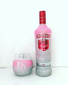 a bottle of vodka next to a wine glass filled with white and pink liquid on a table