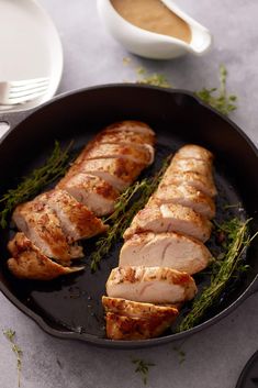 sliced pork in a skillet with herbs on the side and sauces to the side