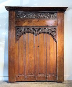 an old wooden door with intricate carvings on the top and bottom panel, in front of a white wall