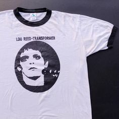 2000's Lou Reed Transformer Ringer T Shirt  CONDITION This vintage Lou Reed T-shirt from the year 2000 is a classic piece. Crafted in white with black ringer details, the shirt is made from lightweight and soft cotton. It's in good condition with minimal cracks and fades on both the shirt and the print. Tagged as size L, for precise sizing, please refer to the provided measurements. The shirt is a blend of 50% polyester and 50% cotton, assembled in Mexico. DETAILS Size On Tag: L Tag: Agusta MEAS Retro White Tops With Band Logo, Retro White Top With Band Logo, Vintage White Top With Band Logo, Vintage White Unisex T-shirt, White Unisex Tops With Band Logo, White Unisex Top With Band Logo, Vintage White T-shirt, Punk Poster, Lou Reed