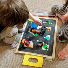 two children playing with toy cars on the floor in front of a play mat that is made out of construction paper