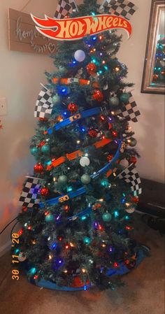 a christmas tree decorated with racing cars and lights is shown in front of a sign that reads hot wheels