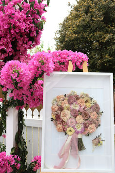 a white frame with pink flowers in front of a fence and trees on the other side