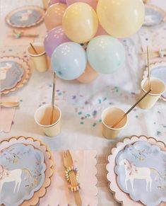 a table topped with plates and cups filled with desserts covered in pastel balloons