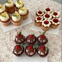 cupcakes and cakes are arranged on white plates with cherries in the middle