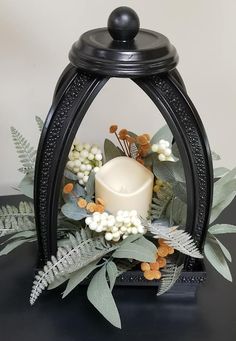 a white candle is sitting on top of some leaves and flowers in a black holder