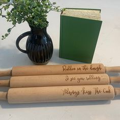 three wooden rolling pins with writing on them next to a book and plant in a vase