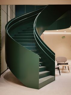 a green spiral staircase next to a chair in a room with white walls and flooring