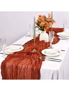 the table is set with white plates and silverware, orange flowers in vases