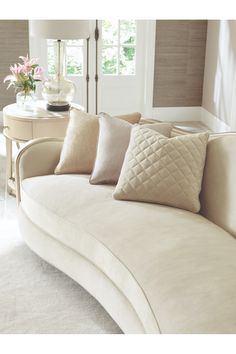 a white couch with pillows on it in front of a table and window sill