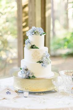 a wedding cake with blue and white flowers on the top is sitting on a table