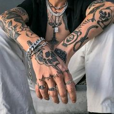 a tattooed man sitting on the ground with his hands crossed and two rings around his wrist