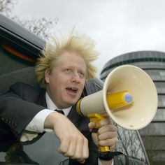 a man with blonde hair holding a yellow and white megaphone while sitting in the back of a car