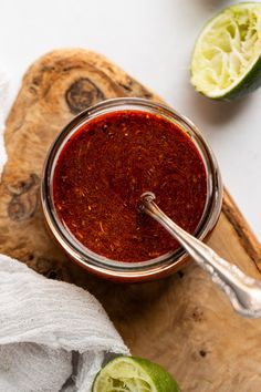 a glass jar filled with red sauce next to an avocado on a cutting board