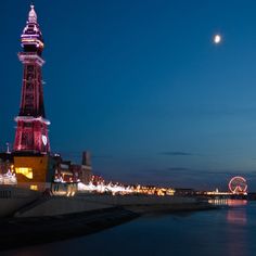 a tall tower with a clock on it's side next to the water at night