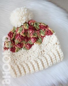 a crocheted beanie with pom - pom on top sitting on a white furnishing