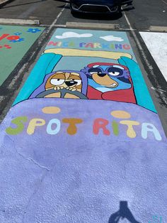 a car parked on the side of a road next to a parking lot painted with cartoon characters