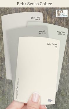 someone holding up some white paint swatches on a wooden surface with text overlay that reads behr swiss coffee