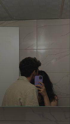 a man and woman taking a selfie in the bathroom mirror with their cell phone