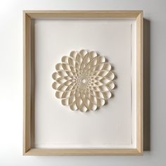 a white paper art piece in a wooden frame on the wall above it is a circular flower