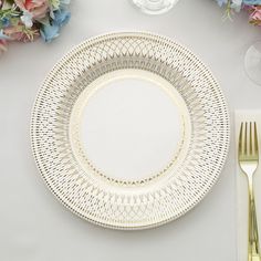 a white plate with gold trim sits on a table next to some flowers and silverware