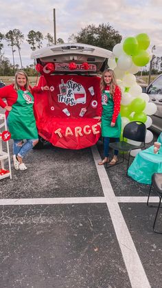 two girls in green aprons standing next to a car with the back door open