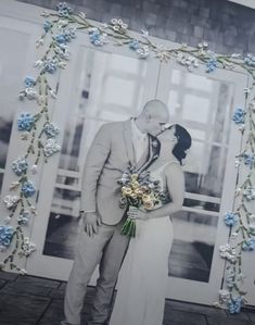 a man and woman standing next to each other in front of a wall with flowers