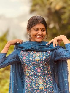 a woman is smiling and holding up her blue shirt with colorful designs on it,