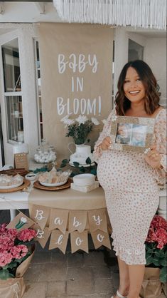 a pregnant woman standing in front of a table with flowers on it holding up a baby in bloom photo