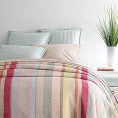 a bed with striped comforter and pillows in a room next to a potted plant