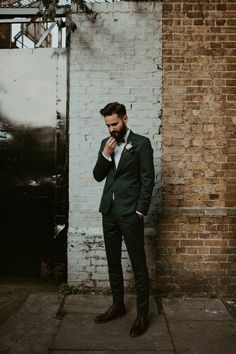 a man standing in front of a brick wall wearing a green suit and bow tie