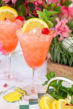 two glasses filled with pink lemonade and garnished with cherries sit on a table