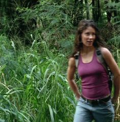 a woman is standing in the middle of some tall grass and trees with a backpack on her back