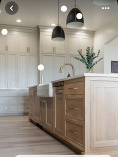 a large kitchen with white cabinets and wood flooring on the walls, along with two hanging lights