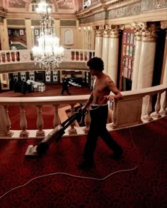 a man with a vacuum in his hand walks down the stairs inside a large building