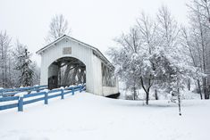 a covered bridge in the middle of winter with snow on the ground and trees around it