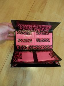 a person is opening a pink box with black designs on the inside and sides, sitting on a wooden floor