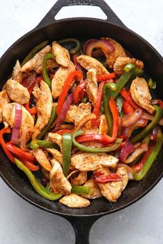 chicken and bell peppers in a skillet on a white counter top with a spoon