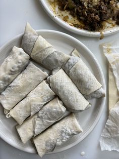 some food is sitting on a white plate next to a bowl of rice and meat