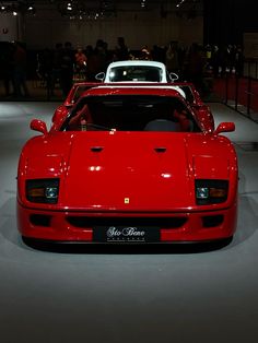 a red sports car is parked in a showroom with people looking at the cars