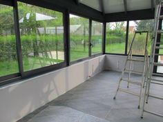 an empty room with large windows and a ladder in the corner next to the window