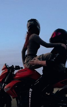 a man riding on the back of a red motorcycle next to a woman wearing a helmet