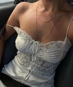 a woman sitting in the back seat of a car wearing a white dress and necklace