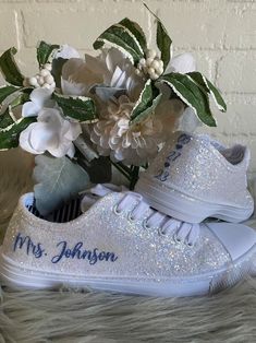 a pair of white tennis shoes with blue lettering on them and flowers in the background