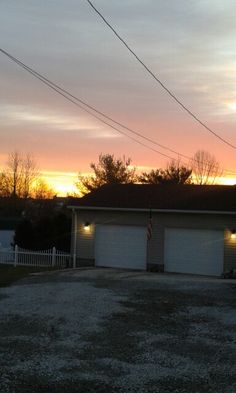 two garages in front of a house with the sun setting behind them and power lines overhead