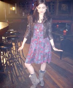 a woman standing in front of a bar wearing boots and a dress with flowers on it