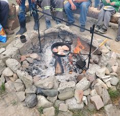 people sitting around an open fire pit with food cooking on it